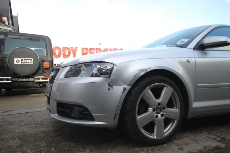 An image of a dented car: silver Audi A3 with a dented, scraped front bumper and wing