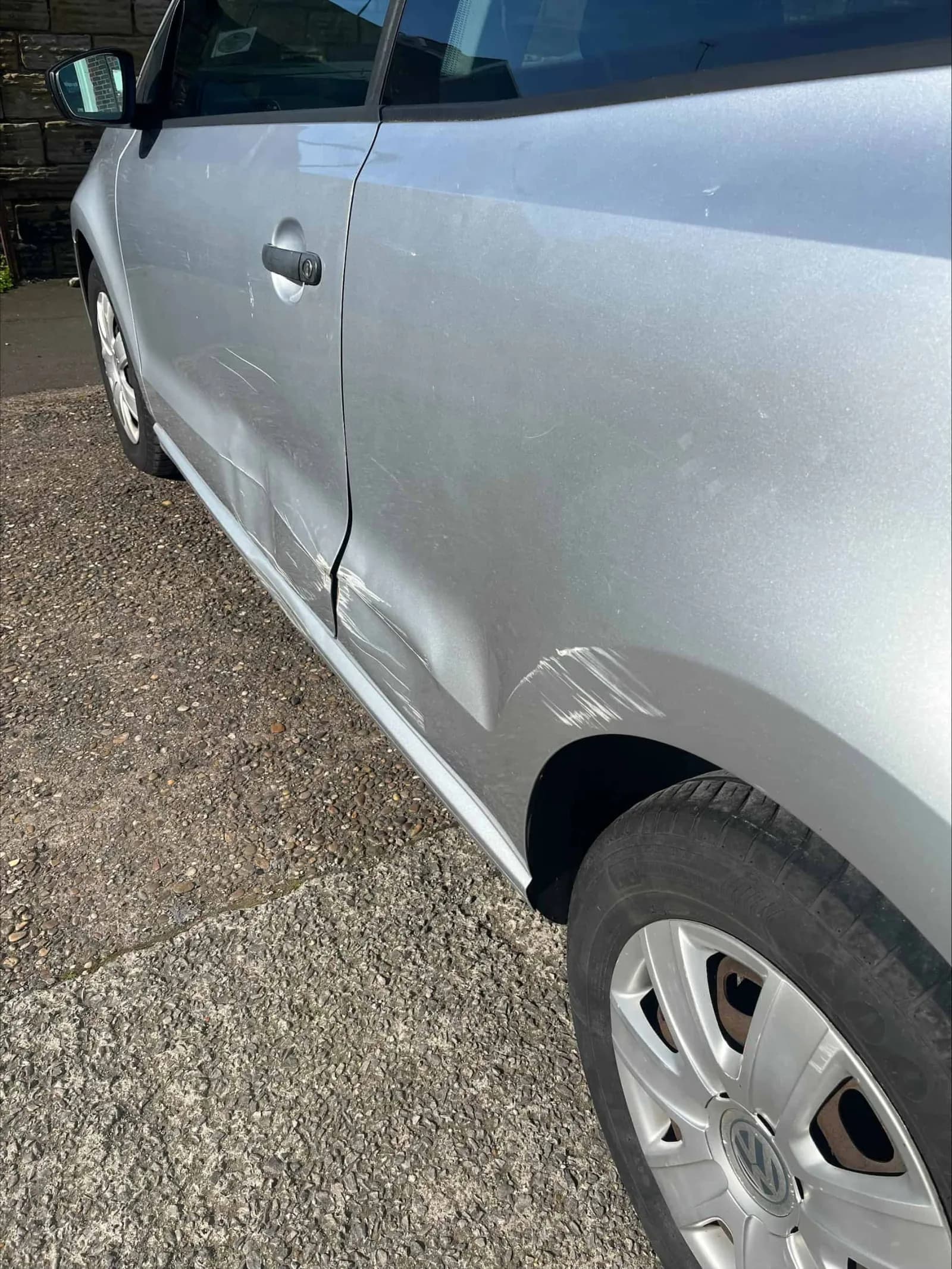 Dent and crease along the rear quarter panel of a silver Volkswagen Polo