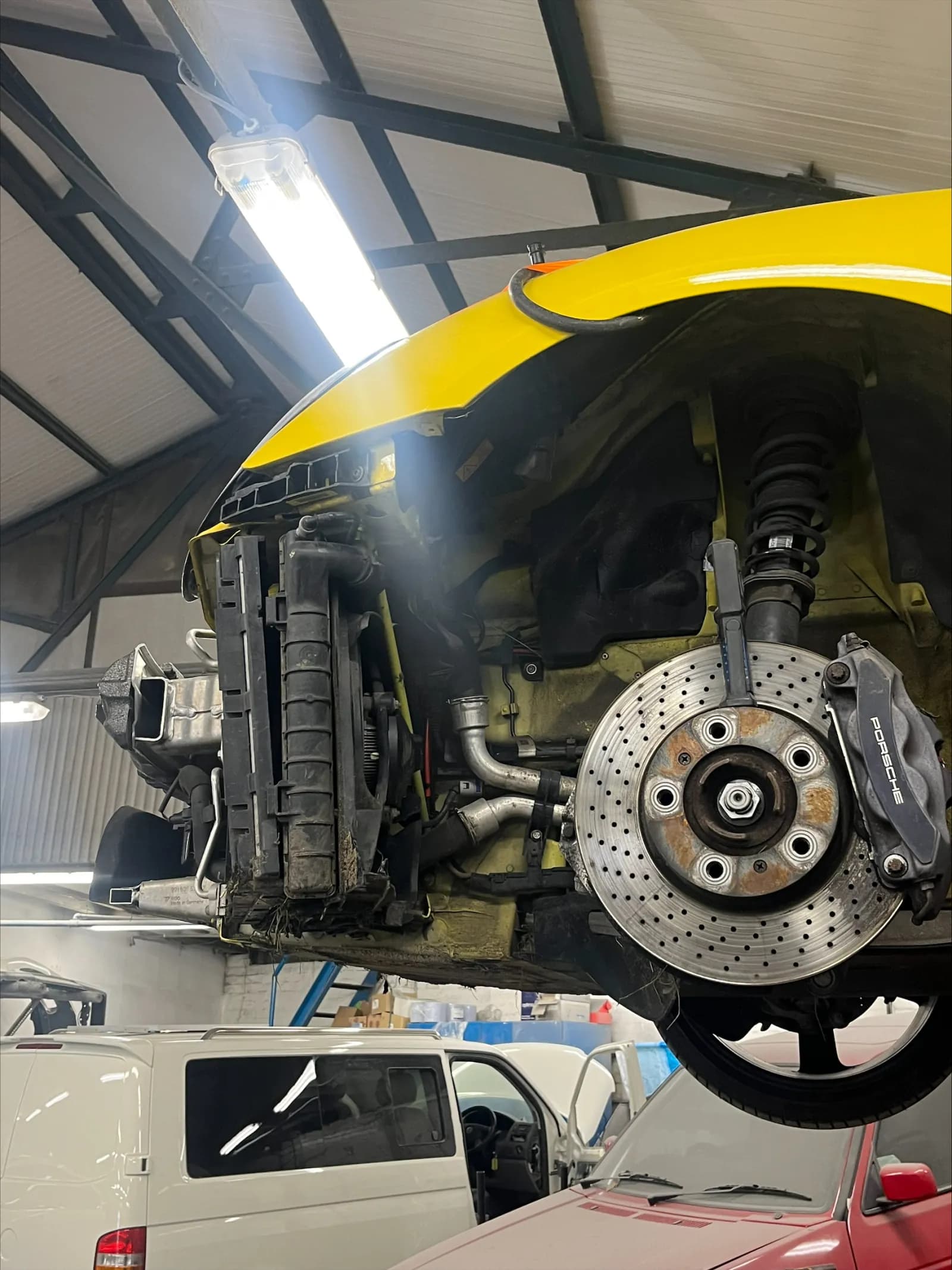 Yellow Porsche Boxster on a lift with the front corner stripped to the brake disc