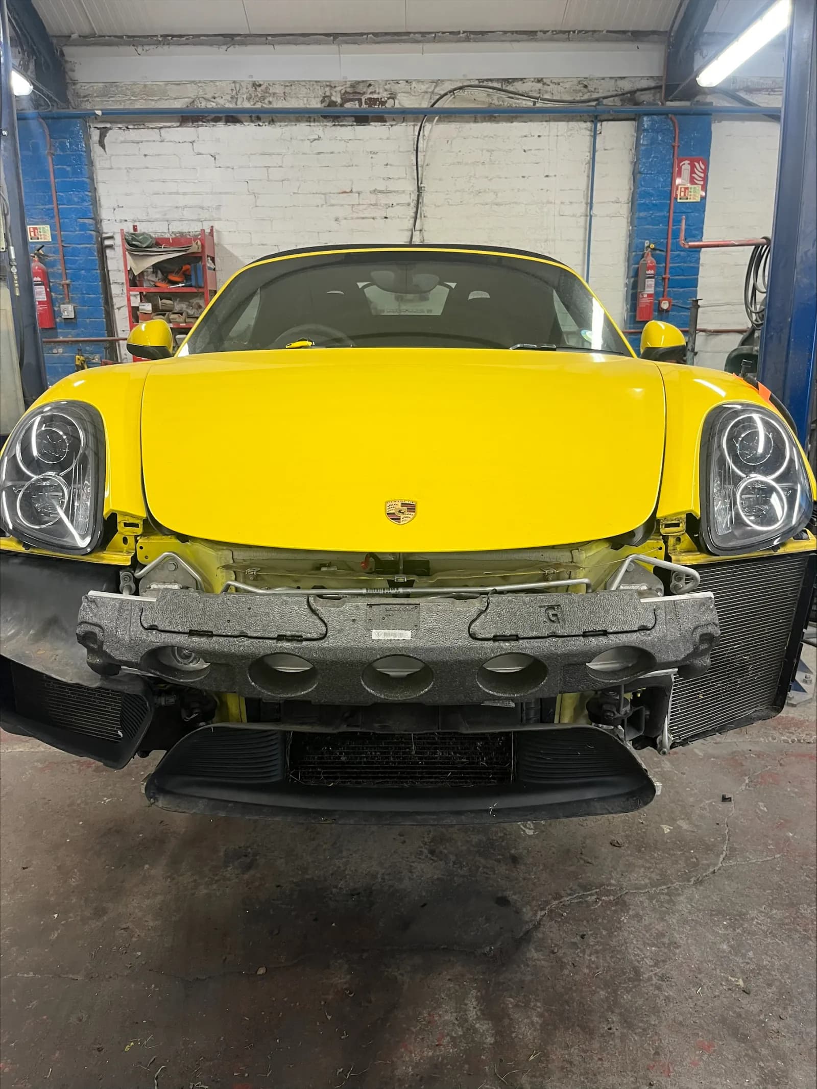Yellow Porsche Boxster in the workshop with the front bumper removed