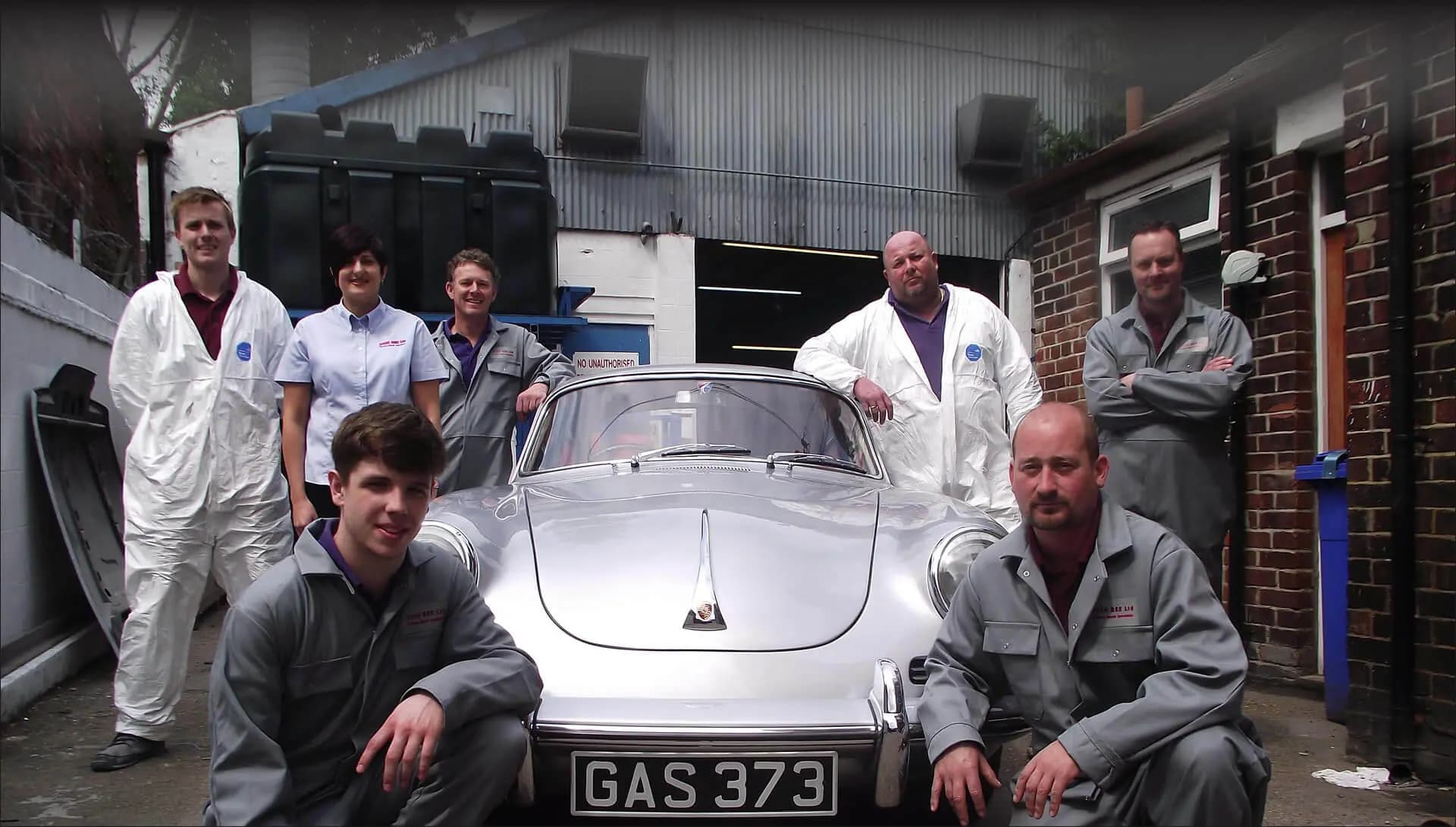 The John Bee team gathered around a silver classic Porsche outside the workshop.